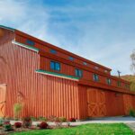 Long side view of a large Monitor style timber frame barn in burnt orange finish, by Harvest moon.